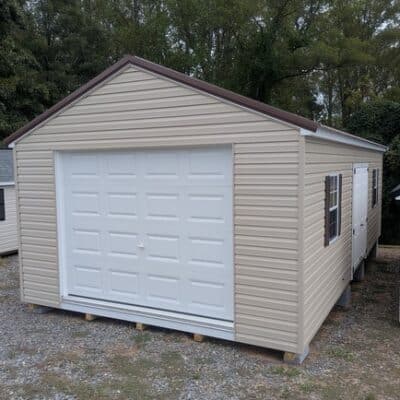 14 x 28 size vinyl a-roof garage style shed with tan siding, white trim, brown metal roof, brown shutters, 9x7 garage door, 6 foot fiber double doors with two windows.